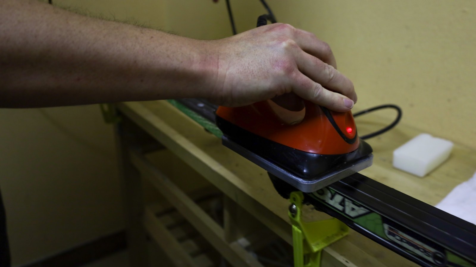 Hand guiding a hot wax iron along a ski base in a workshop (stock placeholder)